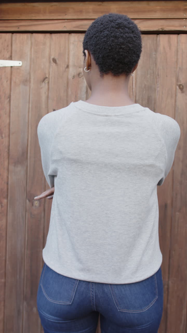 Vertical video of rear view of african american woman in grey sweatshirt against wooden fence