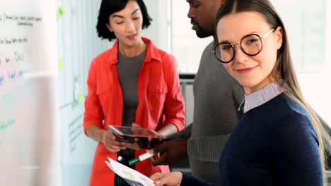 Female-executive-looking-at-document-while-colleagues-discussing-over-whiteboard-4k