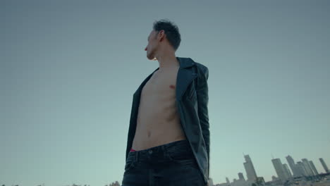 young caucasian man dances on roof with city skyline in background