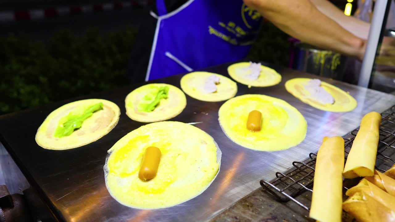 A street vendor crafts traditional crispy pancakes in Bangkok, Thailand. Vibrant lighting highlights the meticulous preparation process