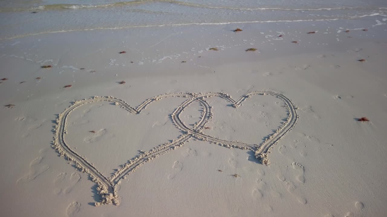 해변에 새겨진 두 개의 맞물리는 심장의 회전 스테디캠 샷