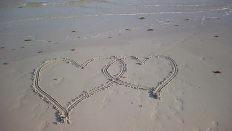 Toma-De-Steadicam-Giratoria-De-Dos-Corazones-Entrelazados-Inscritos-En-Una-Playa