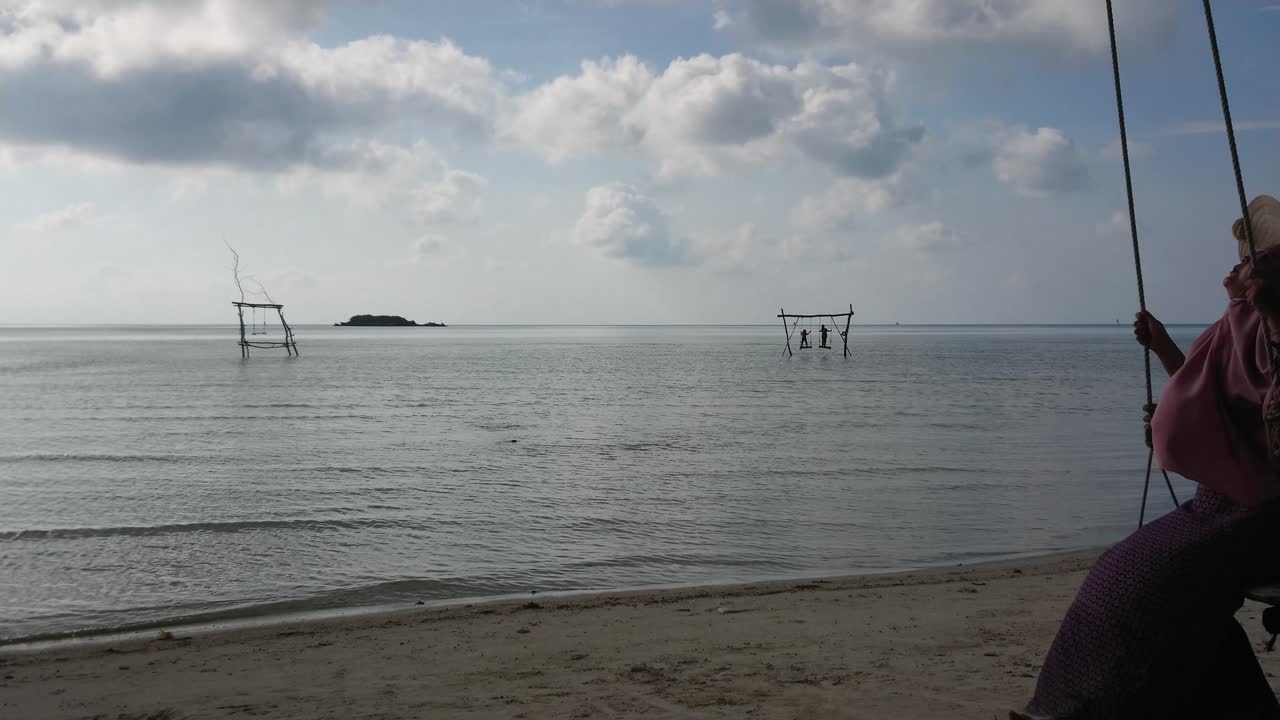 Happy young woman in summer hat swinging on the beach and enjoying sea view