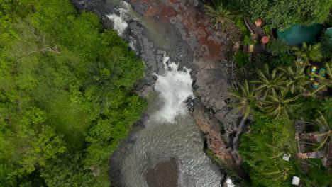 Vista-Aérea-De-Arriba-Hacia-Abajo-De-Un-Río-Selvático-Con-Cascada-Y-Un-Colorido-Restaurante-Al-Aire-Libre-En-Una-Selva-Tropical-De-Bali