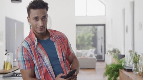 portrait of happy biracial man in sunny modern apartment using smartphone, copy space, slow motion