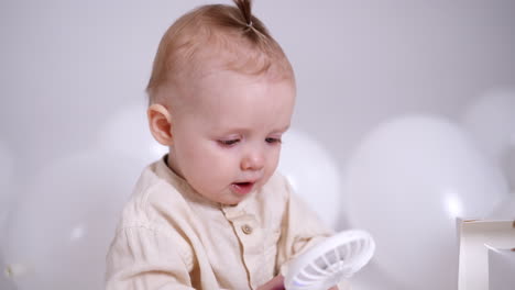 adorable caucasian baby with tiny tail on his head holding a small fan. cute child smiles sweetly to camera. close up.