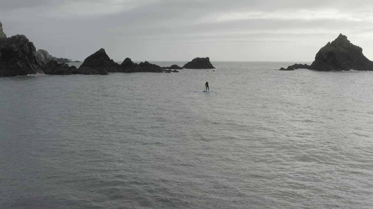 바다 바위 사이의 프레임 중앙에 패들 보더 실루엣을 세우십시오.