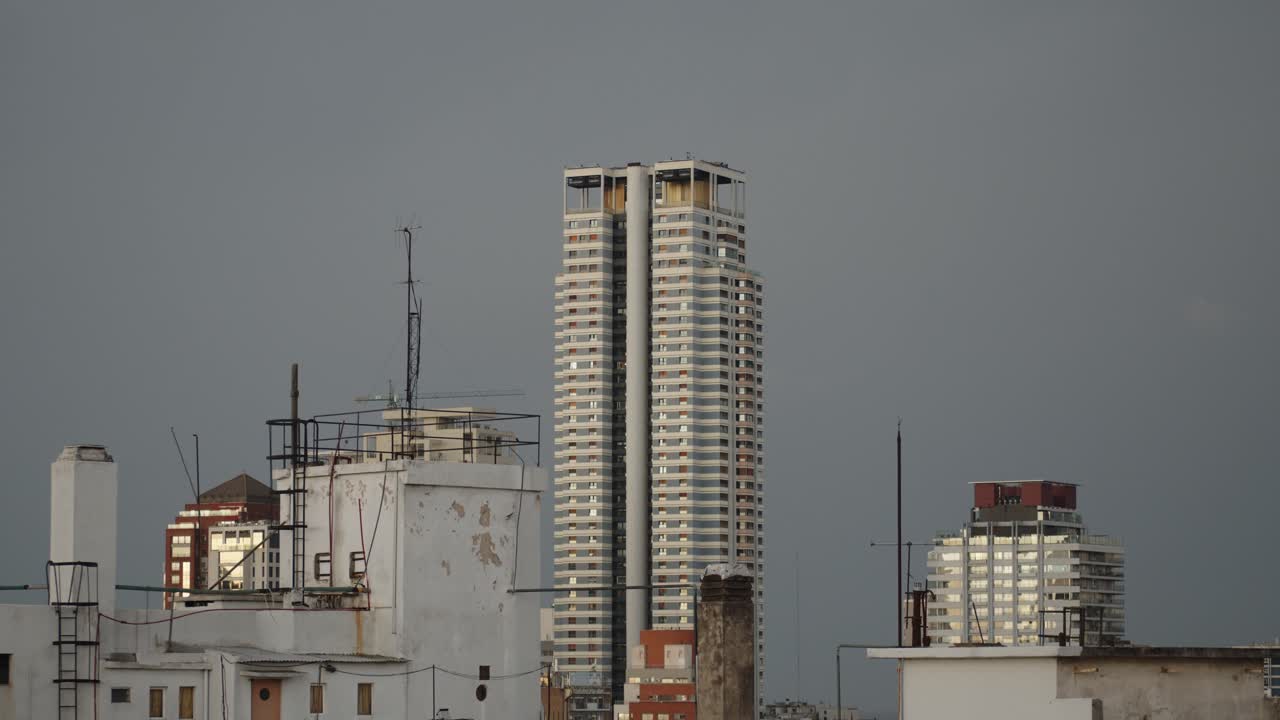 Tall modern skyscraper amid older rooftops in Buenos Aires under an overcast sky