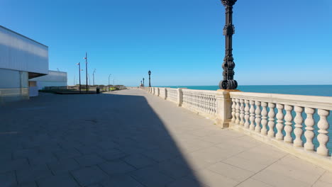 a broad seaside promenade in cádiz with an ornate street lamp and a classic balustrade, offering expansive views of the sea under a clear blue sky