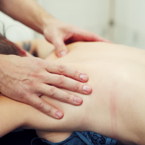 two hands of a professional therapist doing massage on female's back outside. young woman getting body massage while spa and relax therapy in summer.