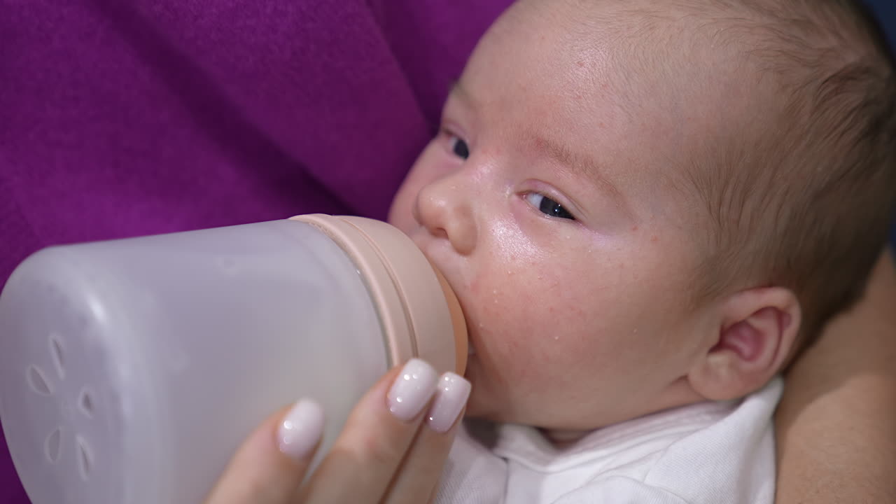 Baby being fed with milk from a bottle. Lovely child is suckling milk and moving his eyes right and left. Close up portrait.
