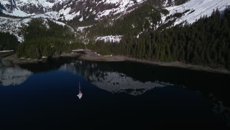 Aerial-view-of-a-sailboat-anchored-under-steep-snowy-peaks-of-Knight-Island,-Alaska