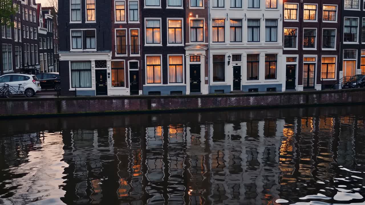 Charming canal-side view of historic buildings reflecting on water, showcasing warm evening light and architectural details in a serene urban setting