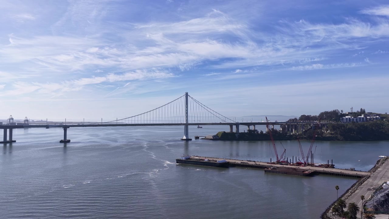 Splendida ripresa aerea panoramica del ponte San Francisco–Oakland Bay in una giornata di sole con nuvole leggere, che mostra la campata sospesa che collega la città a Treasure Island e al suo porto.
