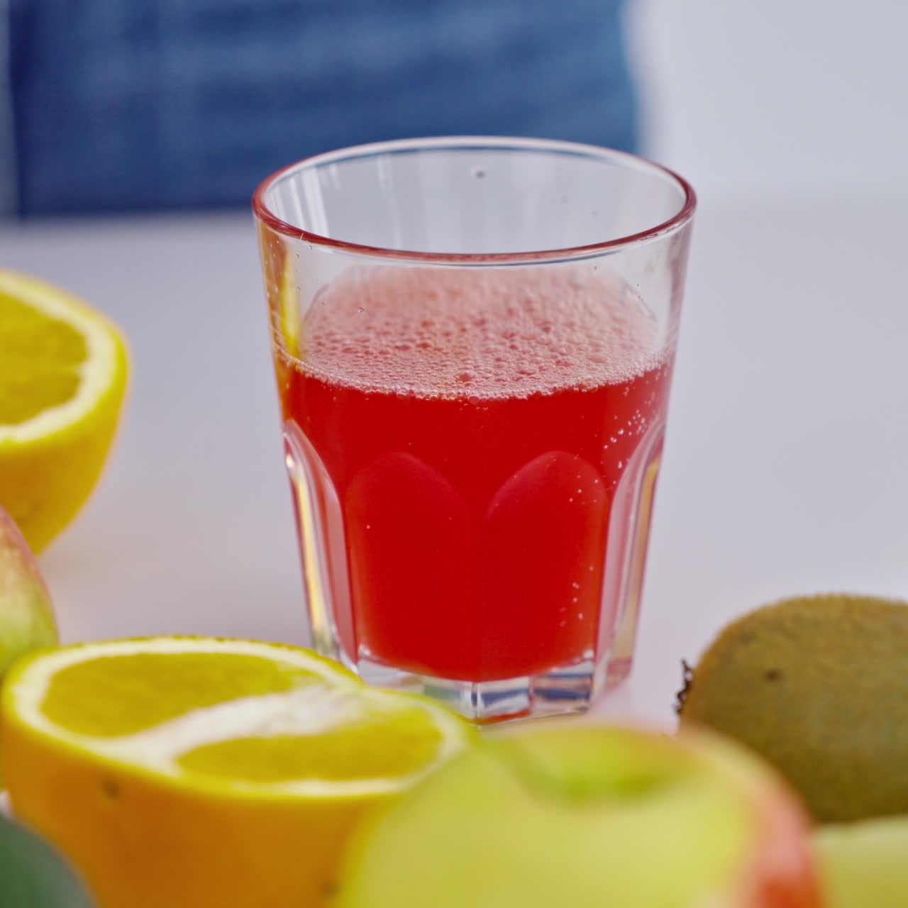 Glass of fresh red juice among fruits. Female's hand taking glass of freshly squeezed juice from the table. Dieting concept. Close-up.