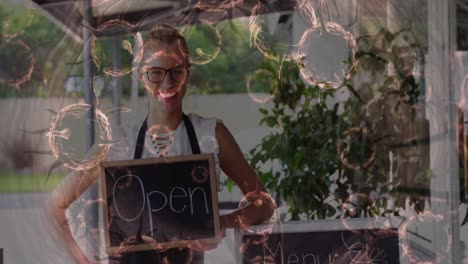 animation of macro covid-19 cells floating over happy caucasian female chef holding open sign