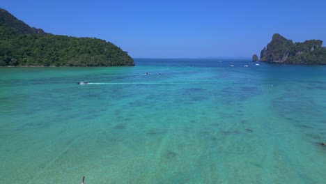 Koh-Phi-Phi-Bay,-colorful-traditional-longtail-boats-are-floating-on-calm-turquoise-water