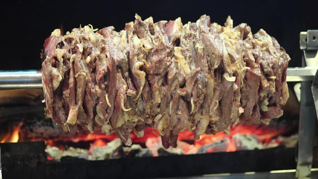 Carne cruda condita che ruota su uno spiedo su carboni ardenti.