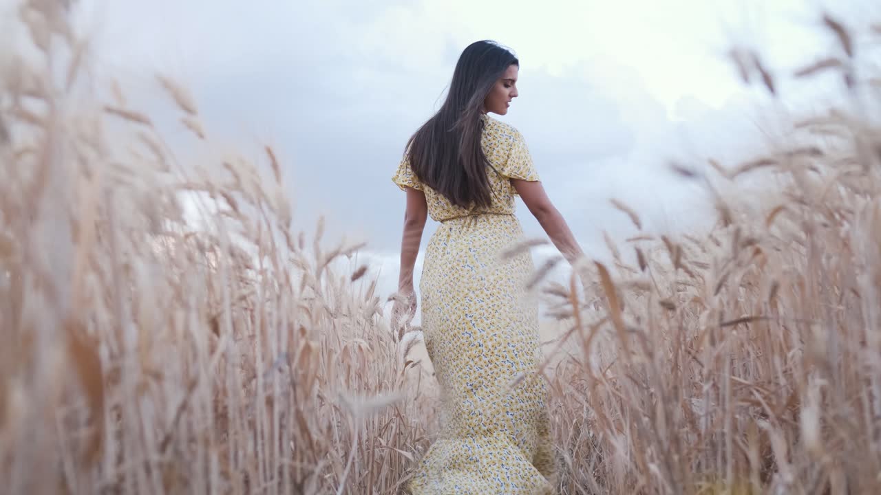 Woman in a dress walking through a wheat field. Nature and agriculture concept.
