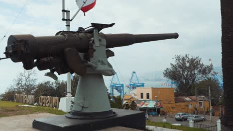 pan a la derecha de una vieja ametralladora del ejército, bandera chilena ondeando en la parte de atrás en el museo marítimo nacional, valparaíso, chile