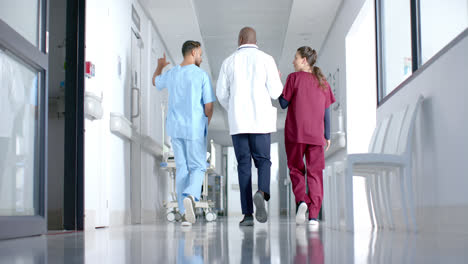 diverse male and female doctors discussing work and walking in corridor at hospital, slow motion