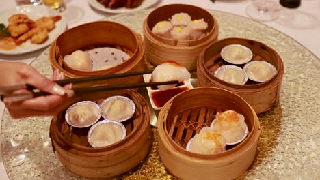 hands use chopsticks to pick dim sum from bamboo steamers on a rotating table, creating a communal dining experience