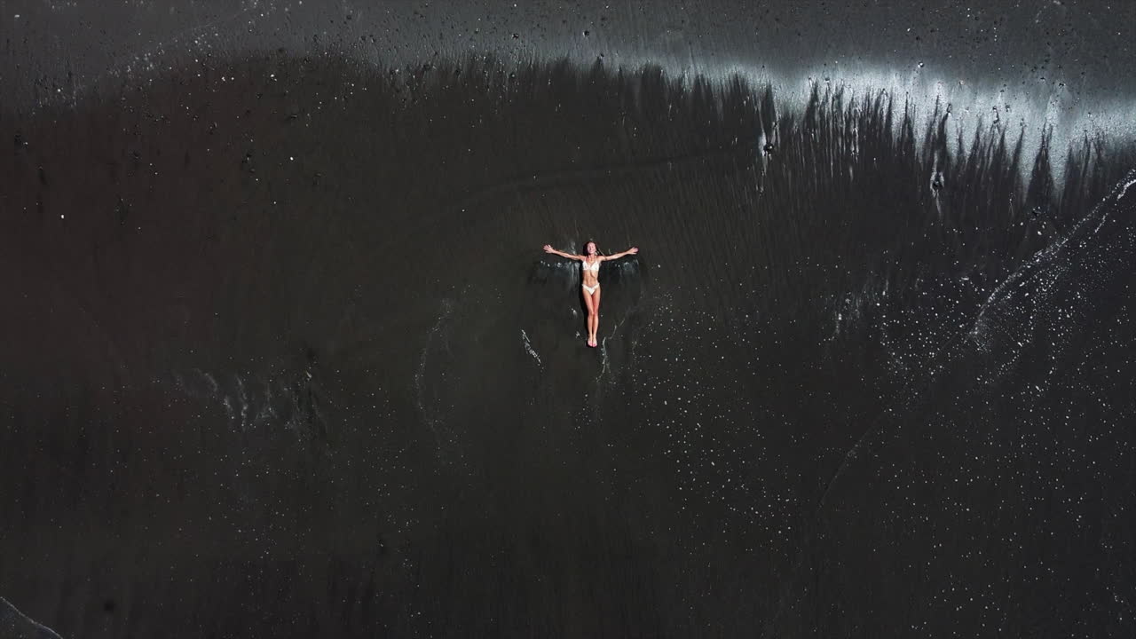 mujer relajándose en una playa de arena negra
