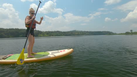 a blonde woman paddles into some reeds on a stand up paddle board on the river nile in africa