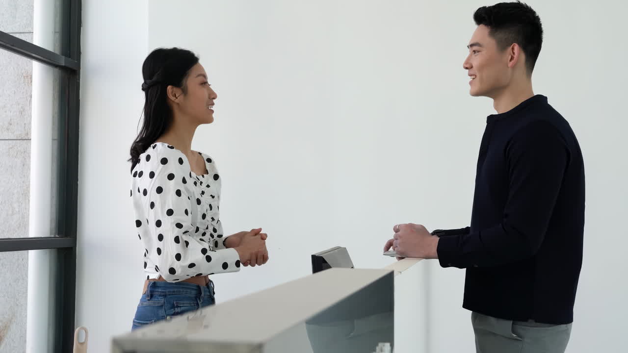 Friendly staff member receptionist standing at the counter to welcome visitors check-in, answer customer questions, provide high quality service in the lobby of a company corporate or hotel.