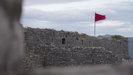 albanian flag waving in the wind at rozafa castle in albania. - wide shot