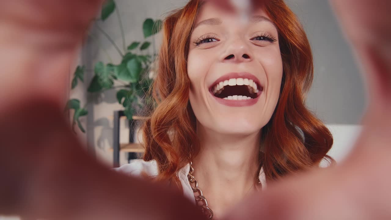 Donna dai capelli rossi innamorata che tiene un segno a forma di cuore con la mano alla vigilia di San Valentino