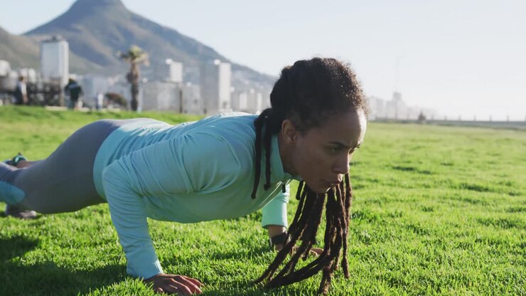 African american woman in sportswear doing press ups in park