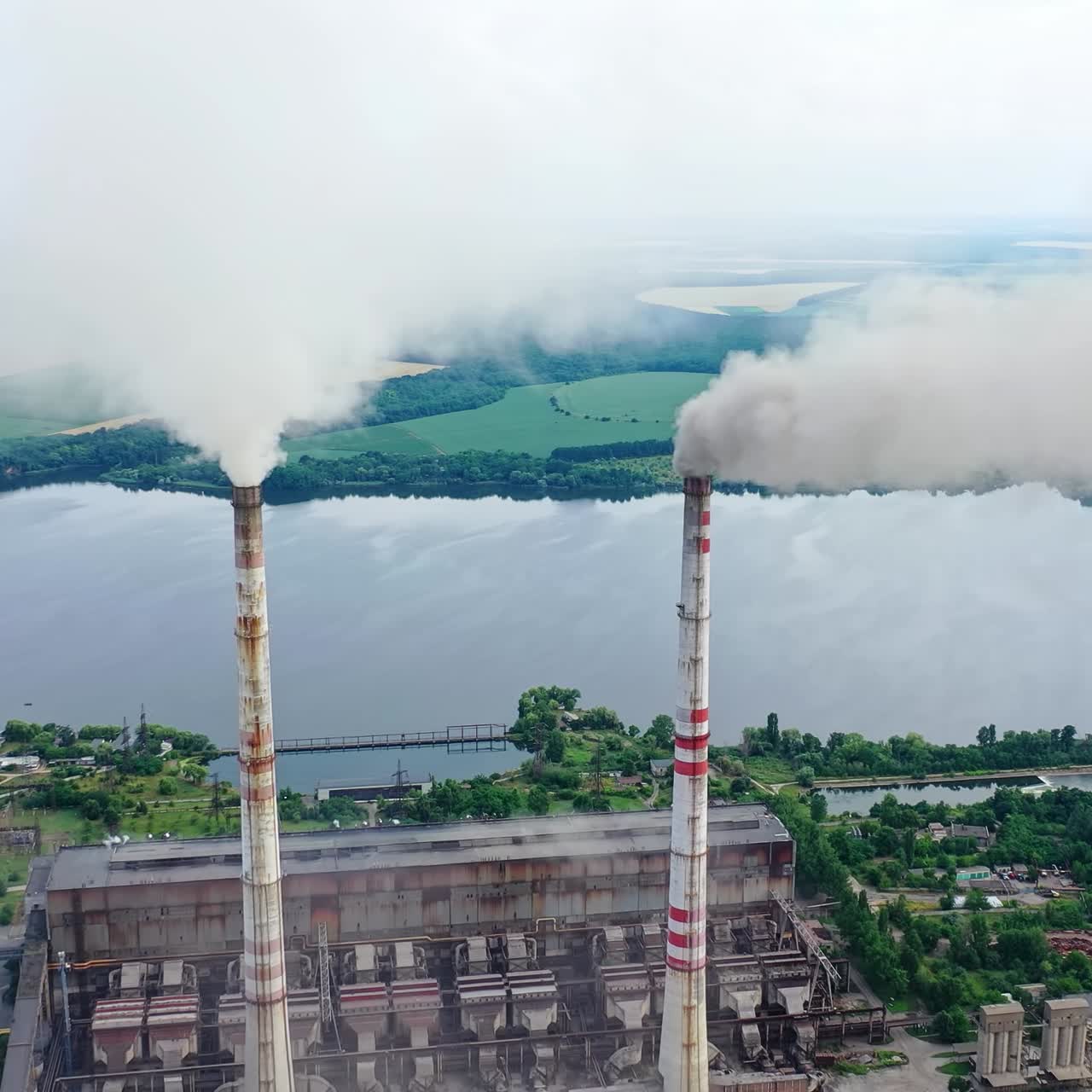 Drone shot of industrial zone with thick smog and burning fossil fuels. Factory zone pan shot left to right of polluted city, many factory chimneys in city area