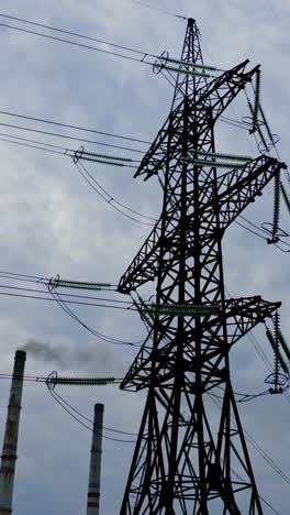 electrical pylons near the industrial pipes. high voltage electrical lines on the evening sky background. smoke from manufacture pollute the air. vertical video