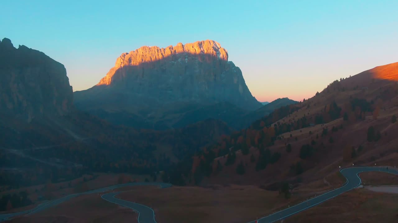 The sunrise illuminates the top of a mountain in the distance as it passes over Gardena Pass and mist in the Dolomites.
