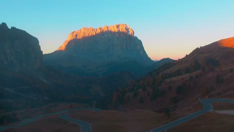 the sunrise illuminates the top of a mountain in the distance as it passes over gardena pass and mist in the dolomites.