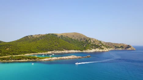 Drone-shot-of-a-speed-boat-cruising-at-its-top-speed-along-the-coastline-of-Cala-Agulla,-a-tourist-destination-in-the-Llevant-Peninsula,-in-Mallorca,-Spain