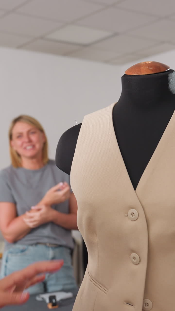 Designer checks vest details meticulously, Model wears buttoned vest in tranquil studio environment, Closeup of fashion designer adjusting vest with textured fabric and buttons in serene studio
