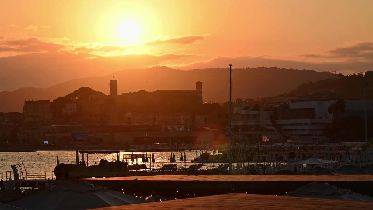 View of the Mediterranean sea coast in Cannes at sunset, France. Sun going behind the horizon, sea port, buildings