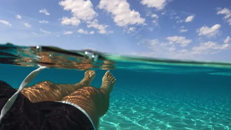 first person view of male legs and feet floating on beautiful clear and transparent ocean water of exotic island