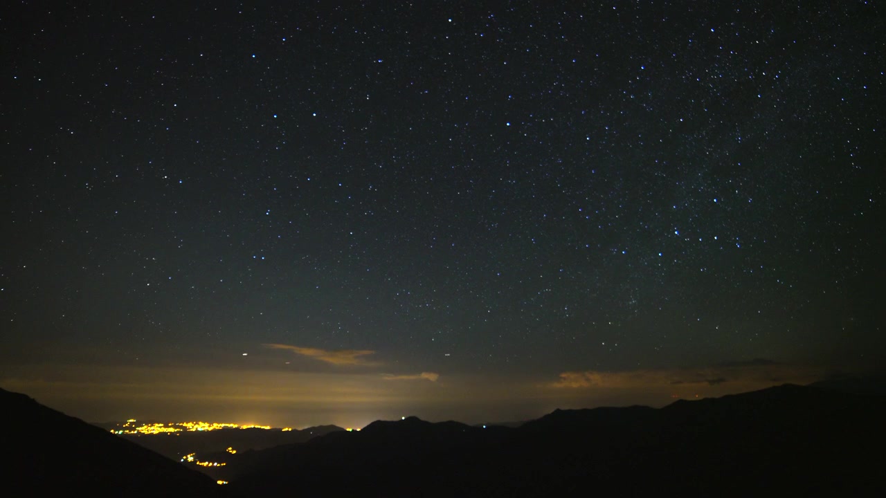 繁星點點的夜空籠罩著遠處城市燈光與山脈剪影