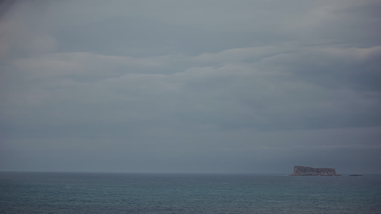 어두운 변덕스러운 날 바다 한가운데에 있는 작은 바위 섬, 타임  ⁇ 스 뷰