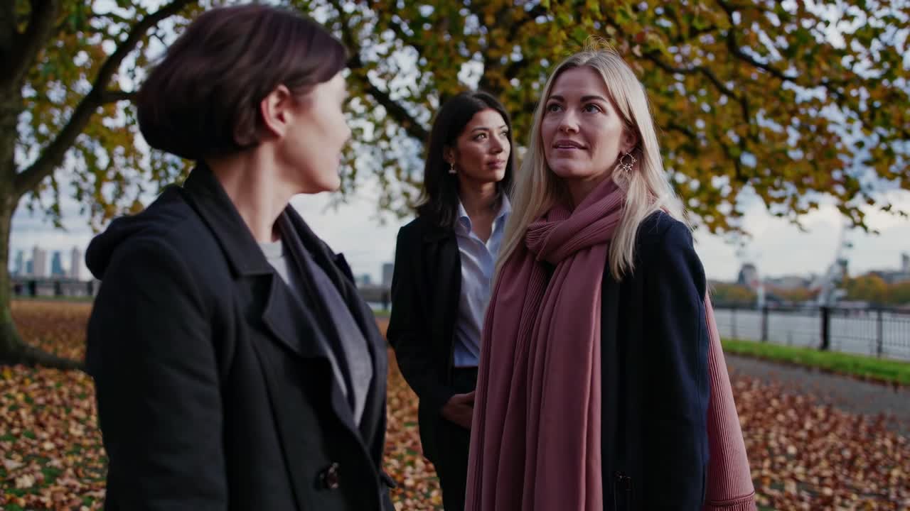 A candid video still of three women in autumn attire, captured from a low angle