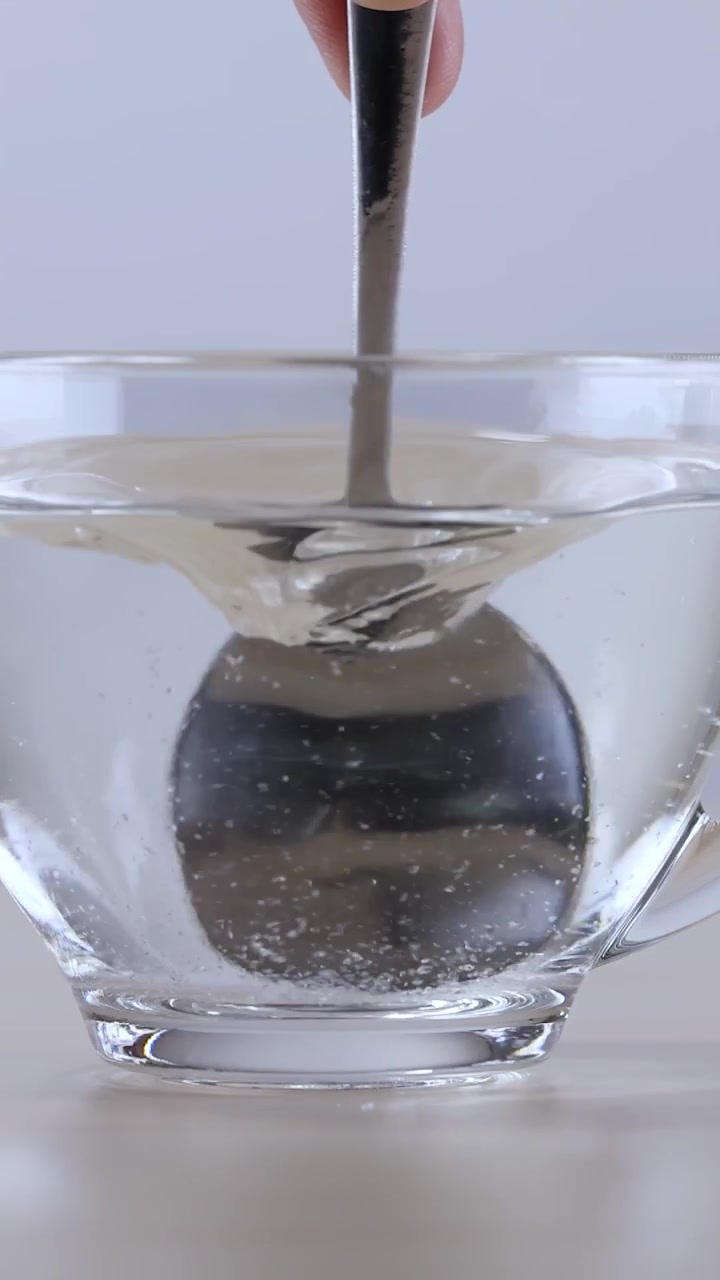Primo piano di un cucchiaio di metallo che mescola polvere bianca nell'acqua all'interno di una tazza di vetro trasparente