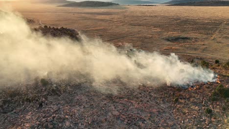 Drone-footage-of-a-Wildfire-ignited-by-a-lightning-strike-on-top-of-a-hill-during-a-thunderstorm,-capturing-intense-flames-and-smoke