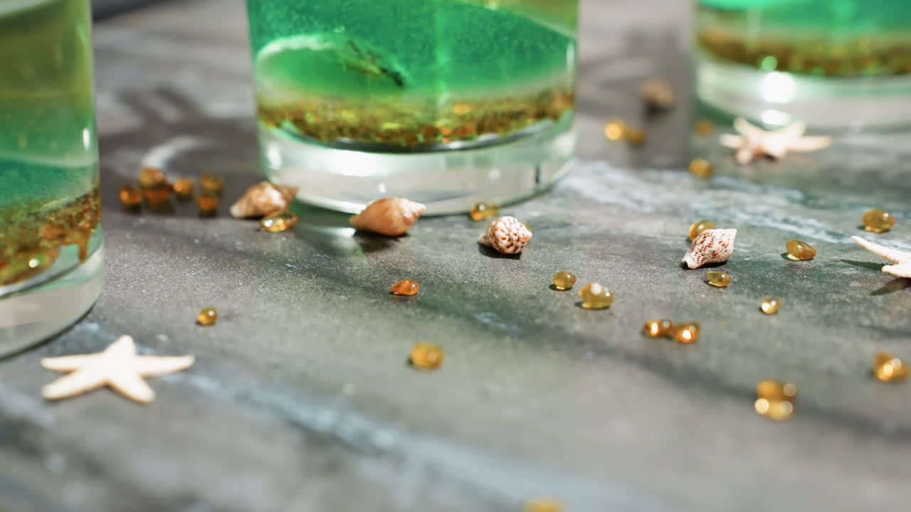 Brown and golden decorative materials including small beads, mini seashells, and star-shaped items scattered across kitchen bench beside tealight cups with green wax mixture