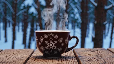 a steaming mug with snowflake design on a wooden table in a snowy forest