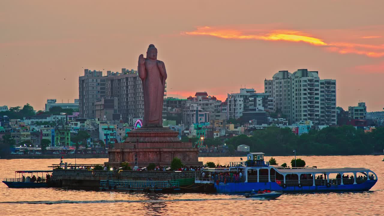 buddha statue with flying birds, golden sky, Boats and crowded residential buildings at Tankbund, hyderabad, telangana, india. Stable Shot, 4k.