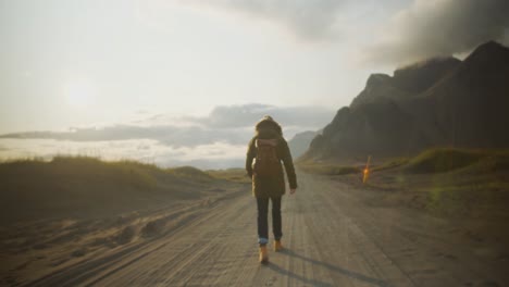 joven caminante camina por un largo camino a la luz del sol poniente en un paisaje montañoso