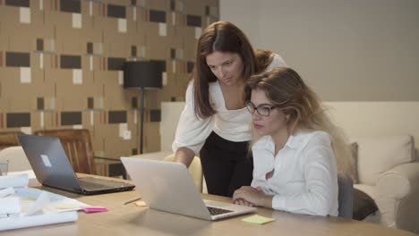 dos colegas mujeres con laptop, hablando en la oficina